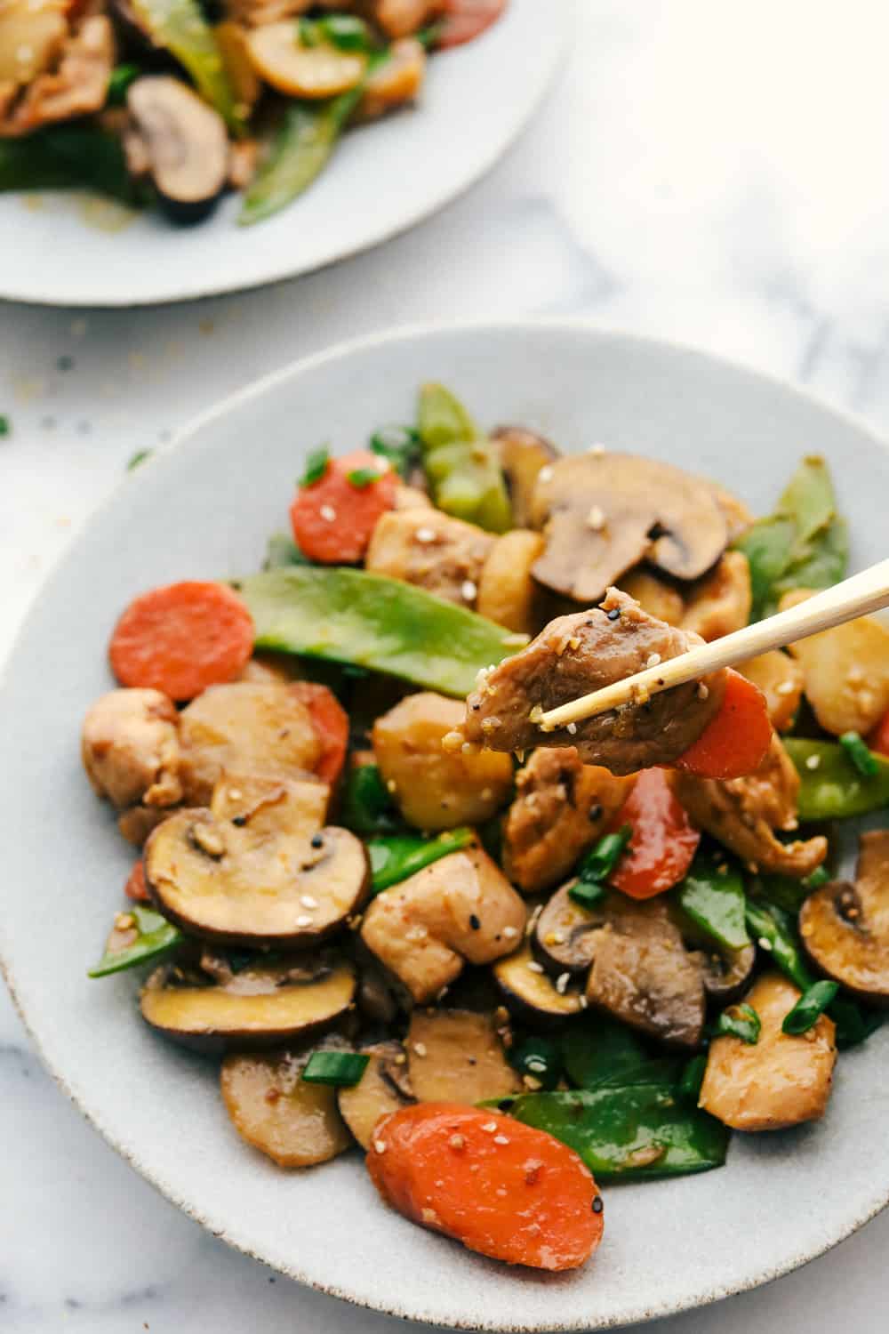Moo Goo Gai Pan is a classic Chinese dish with tender chicken pieces and mushrooms then add in crisp vegetables such as carrots, water chestnuts, snow peas all stir fried together with a special white sauce poured over top and simmered all together. Way better than take out and only 20 minutes! Moo goo gai pan on a white plate.