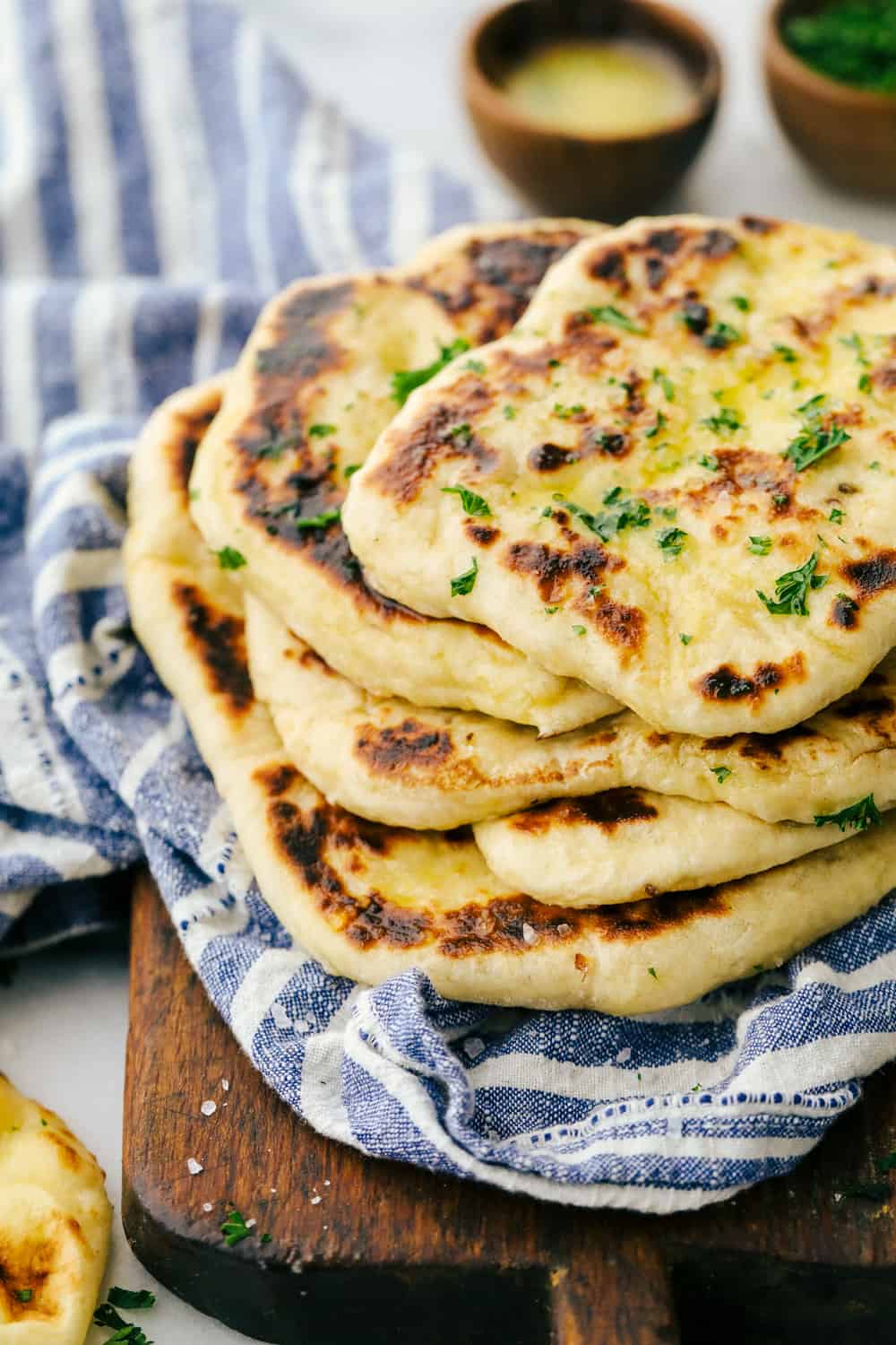 Naan bread stacked on a cutting board with a blue striped towel.