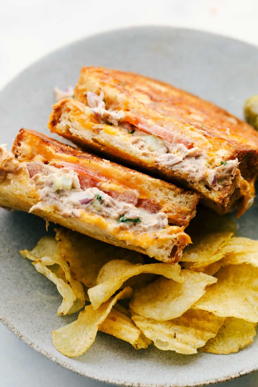 Sándwich de atún derretido sentado en el plato para que veas las capas fundidas juntas con un lado de papas fritas.