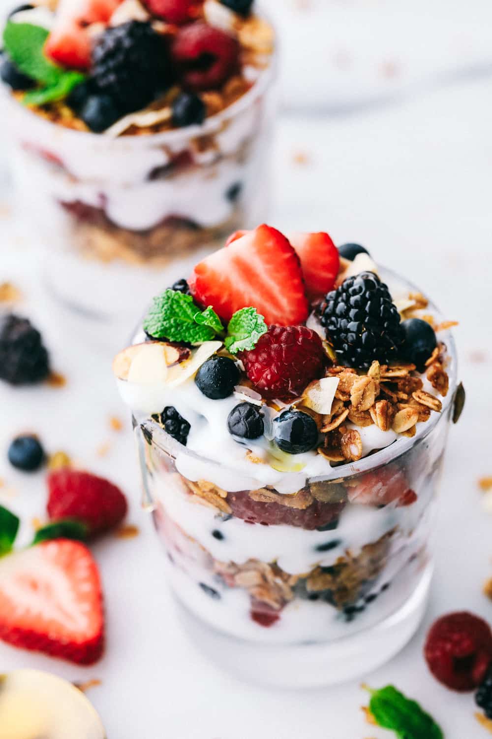 yogurt parfaits layered in glass cups garnished with mint and berries spread around the glass cups for display.