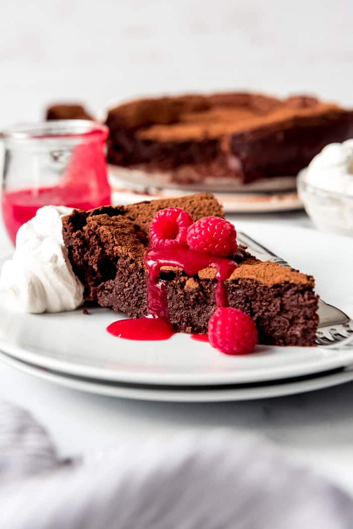 Una imagen de una rebanada de torta de chocolate con frambuesas y coulis de frambuesa en la parte superior.