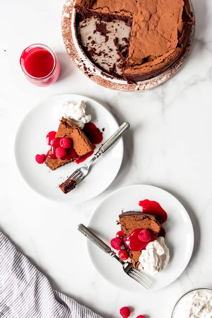 An image slices of chocolate torte on plates with raspberry sauce and fresh berries.