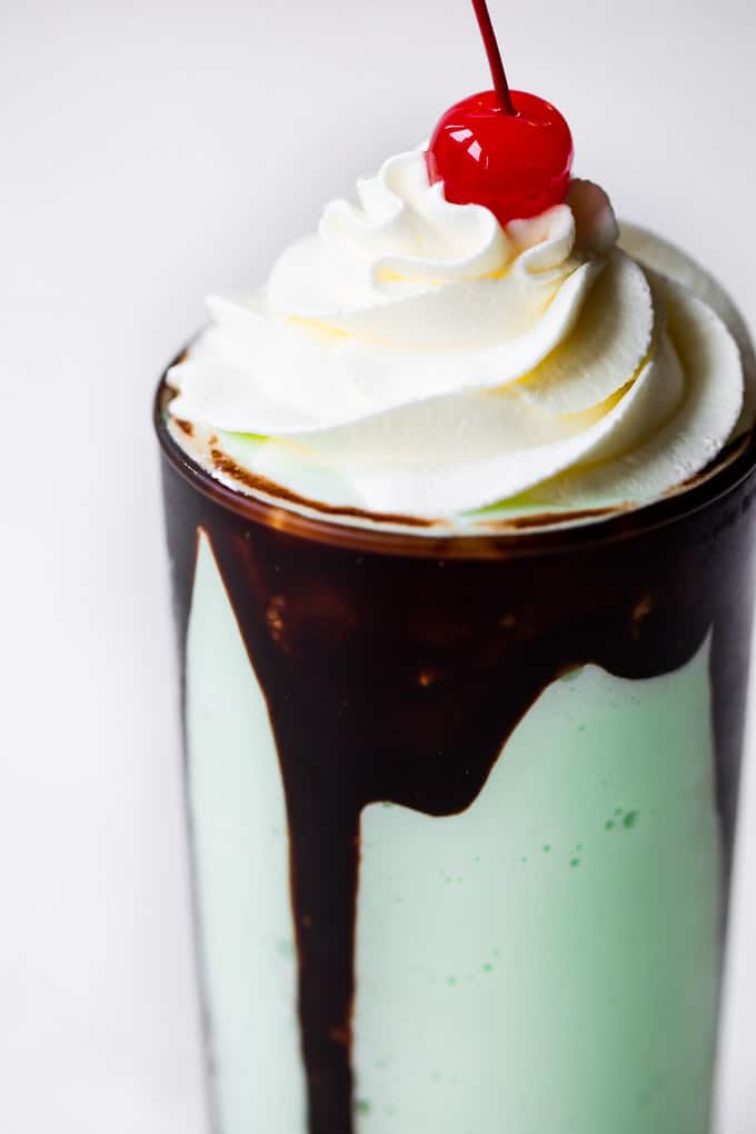 Shamrock shake with chocolate syrup dripping down the sides with whip cream topping and a cherry on top. 