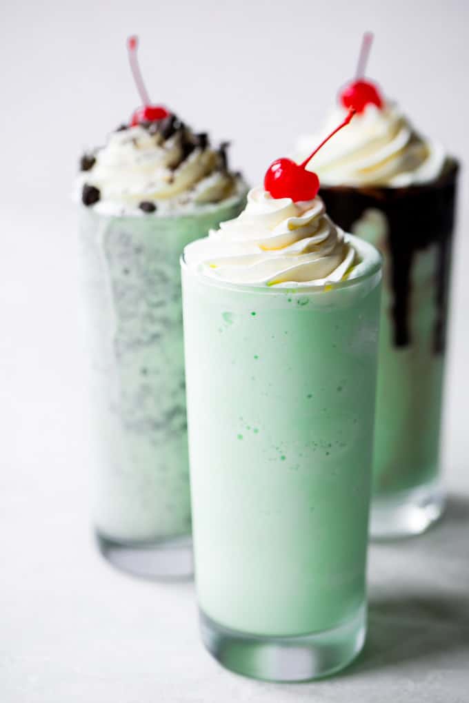 Three tall shamrock shakes with whipped cream and a cherry on top. 