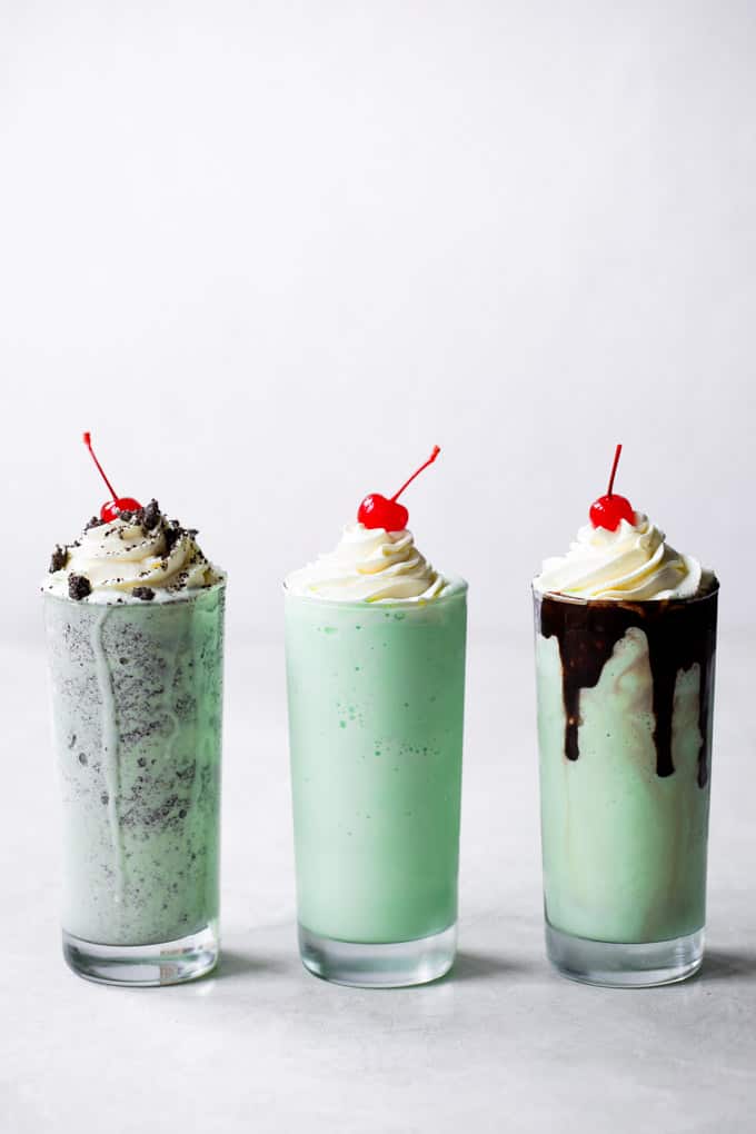 Three tall glasses of shamrock milkshake with whip cream and a cherry on top of each of them. 