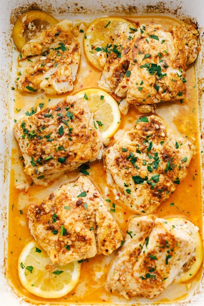 Cajun garlic butter cod baked in a white baking pan with lemon slices.