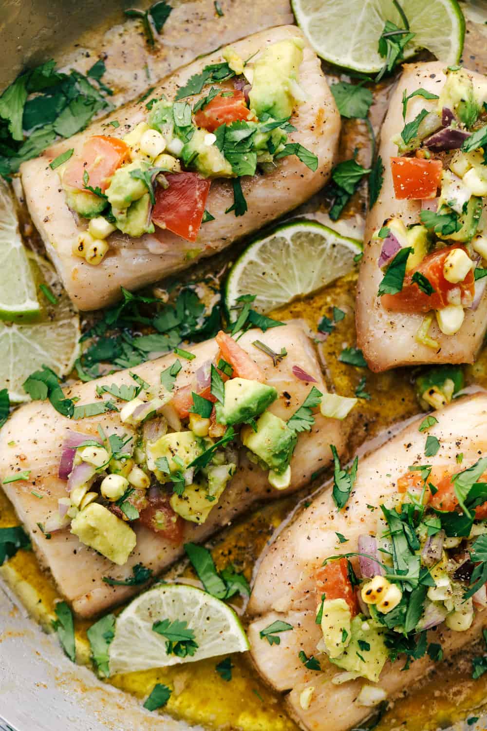 Mahi Mahi filets ina skillet with the brown butter sauce and garnished with avocado salsa with lime wedges in the skillet. 