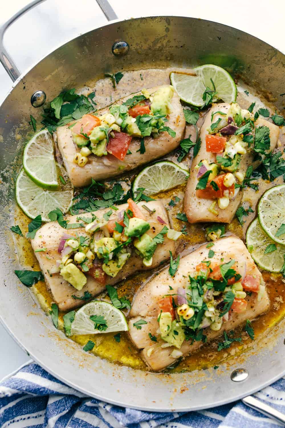 Mahi Mahi filets cooked in a skillet with brown butter and garnished with avocado on top.