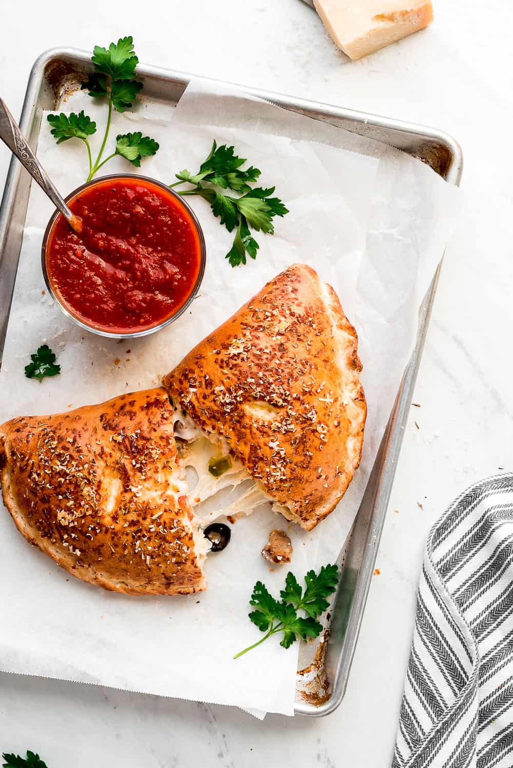 A Calzone cut in half on a baking sheet with a bowl of marinara sauce for dipping.