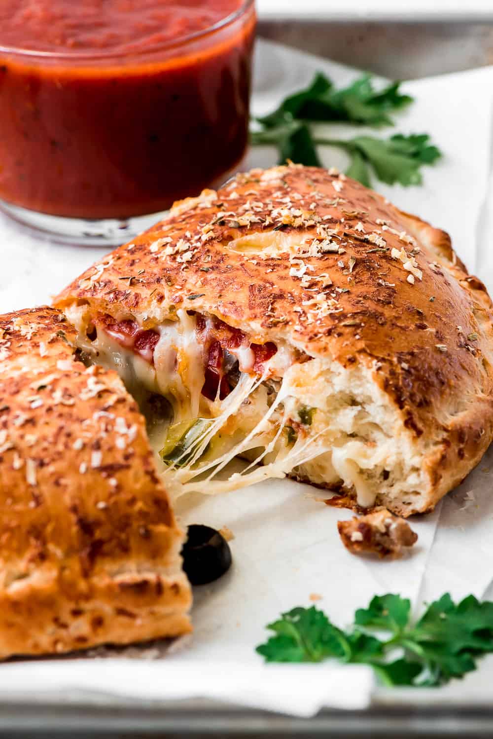 A close-up of the inside of a Calzone cut in half with melted cheese, pepperoni, olives, and sausage.