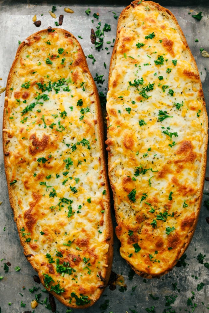 Two cheesy garlic bread pieces next to each other on a pan. 