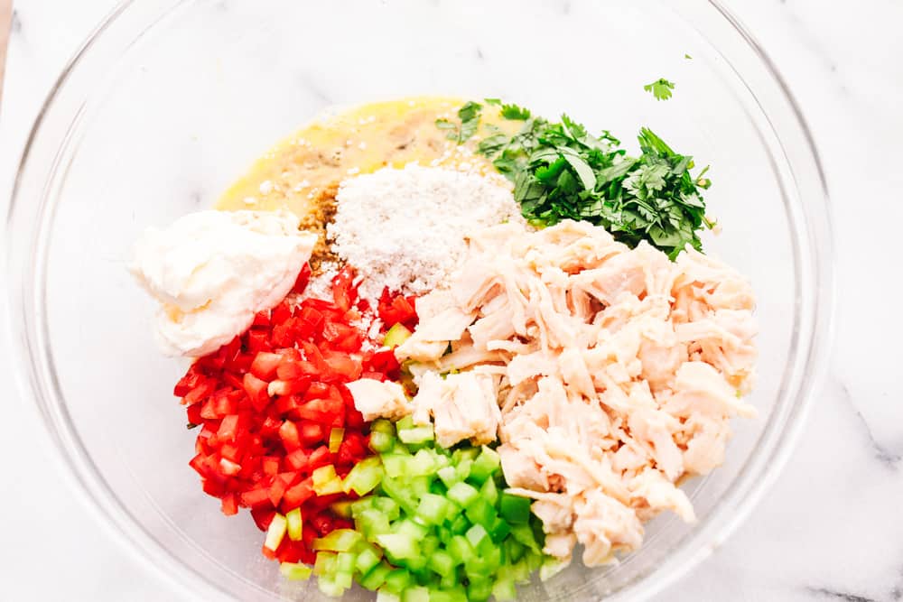 Chicken, bell peppers, garlic powder, beaten egg, mayonnaise and parsley all in one glass bowl. 