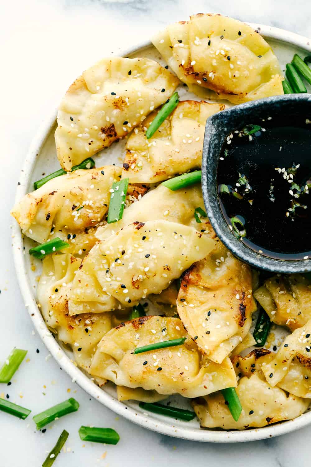 Potstickers on a plate with soy sauce as dipping sauce and scallions garnished overtop. 