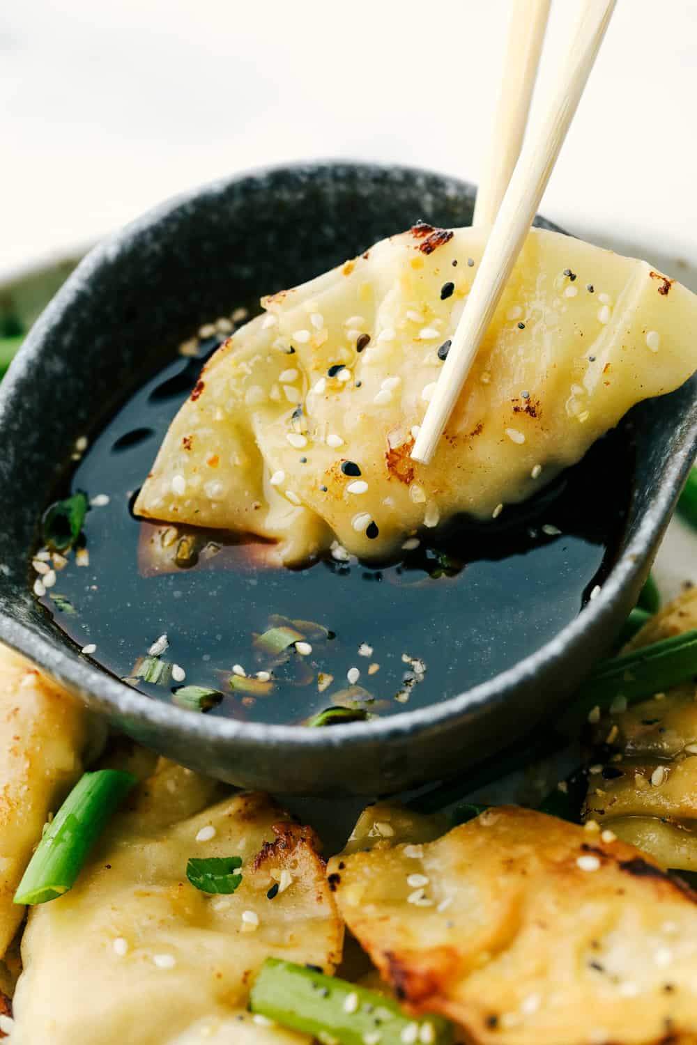 Chicken potstickers on a plate and one being dipped in soy sauce with chopsticks. 