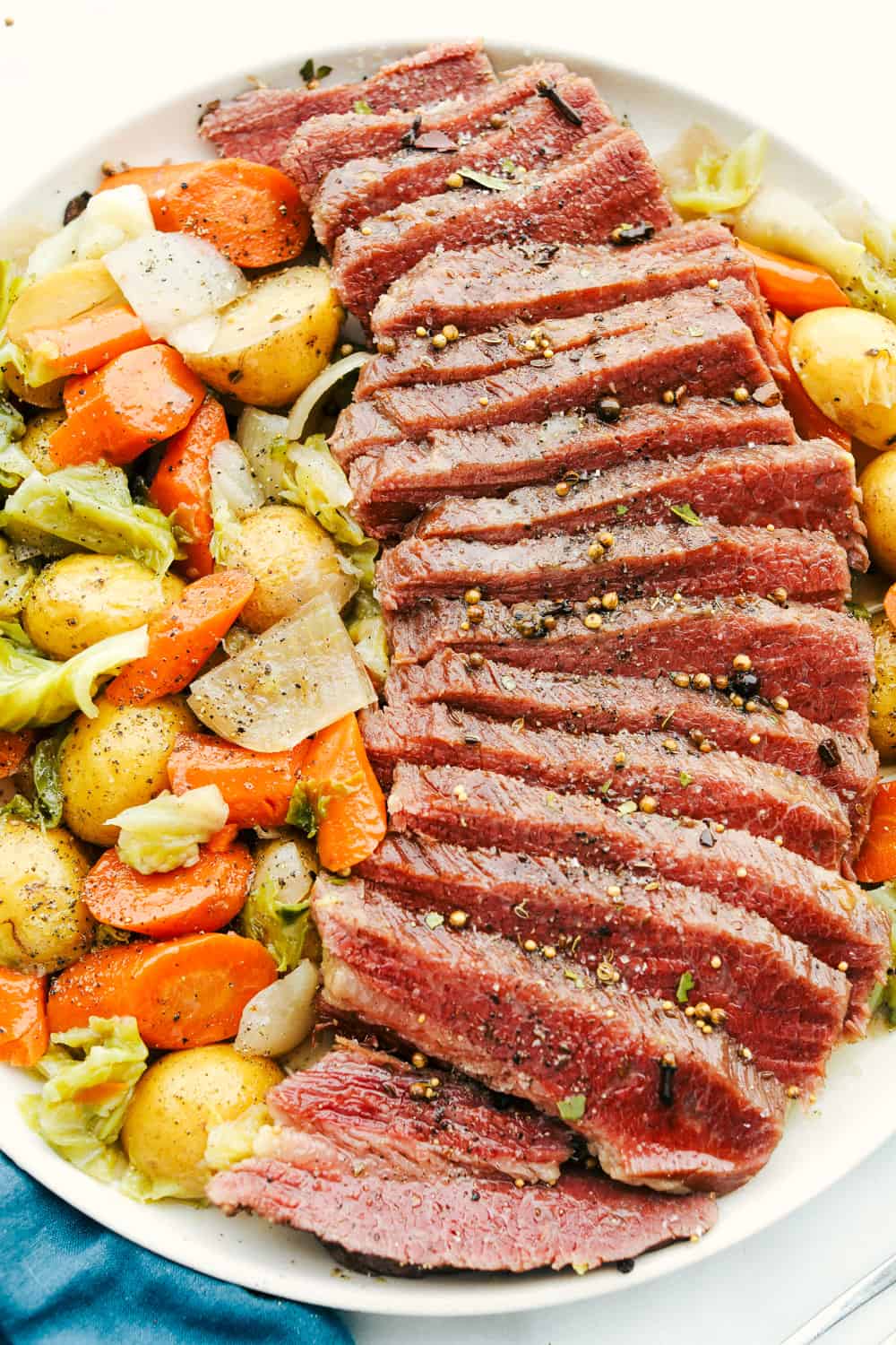 Corned beef sliced in a row with potatoes, carrots and cabbage on the side. 