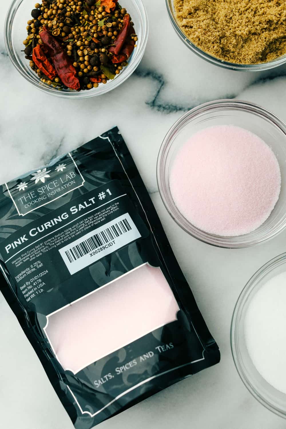 Pink curing salt #1 in a bag and bowl next to it with seasonings and brown sugar in bowls. 