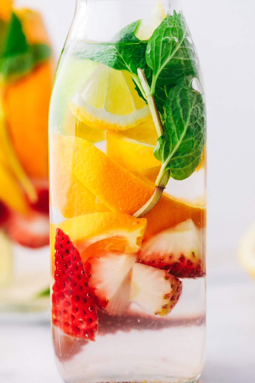 Up close photo of a glass jar with oranges, strawberries, mint and cucumbers. 