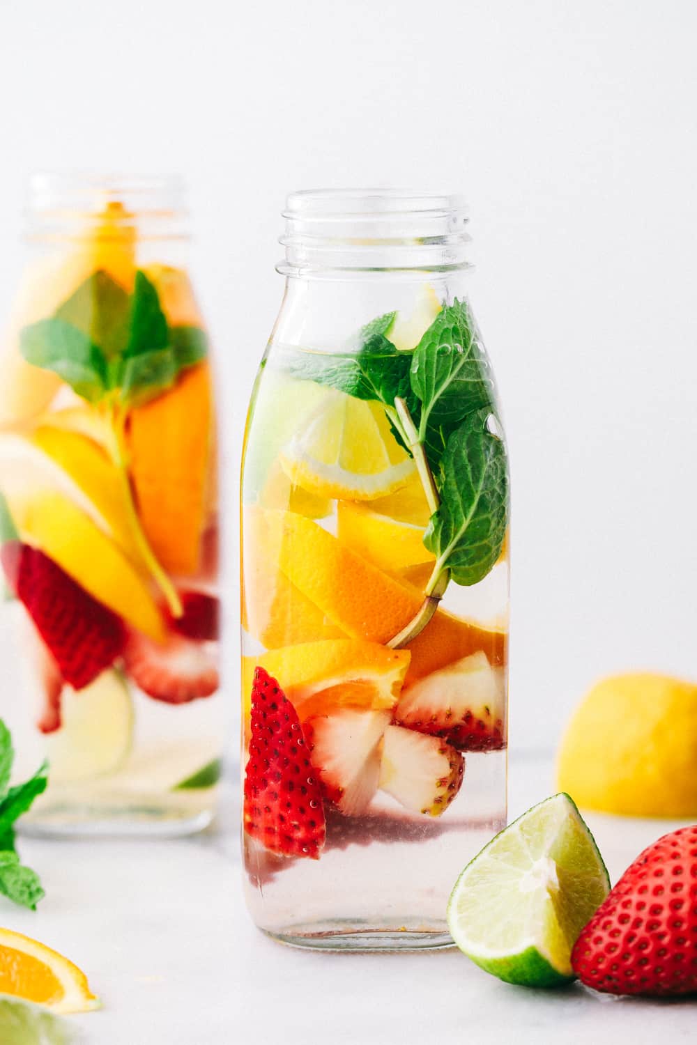 Detox-Wasser in einem Glasgefäß gefüllt mit Zitrone, Limetten, Erdbeeren und Minze. 