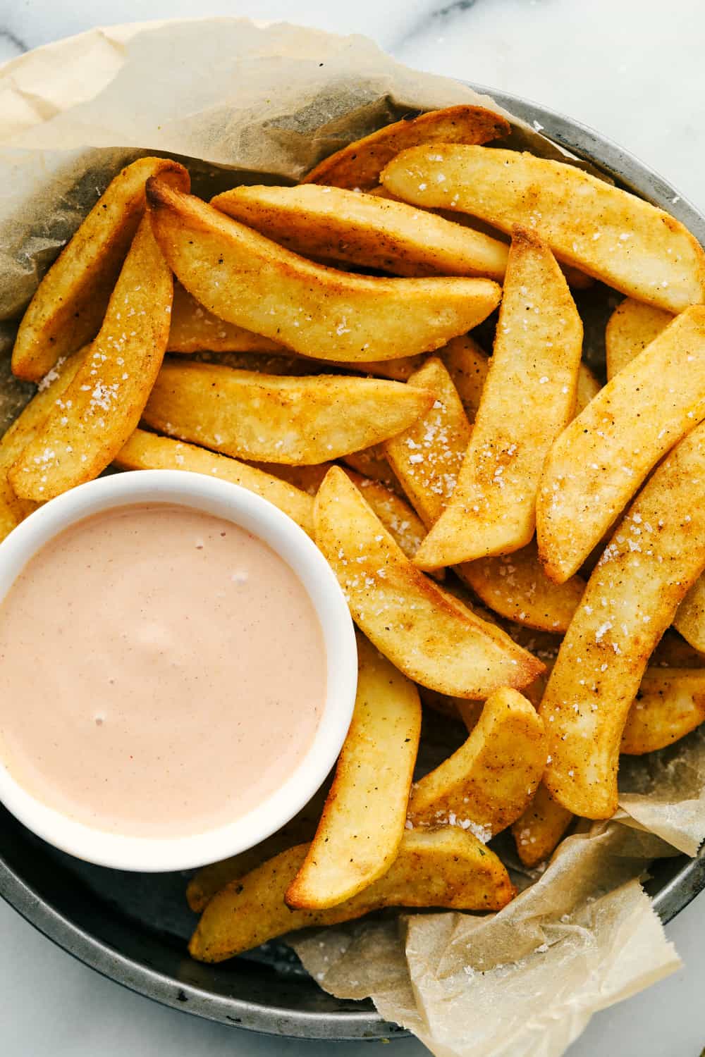 Fries in a bowl with fry sauce in a white ramekin all inside a large plated bowl. 