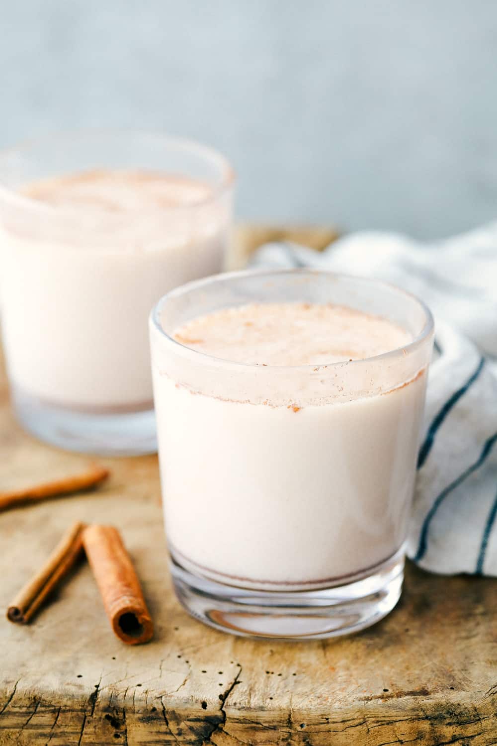 Two glasses full of horchata with cinnamon sticks laying next to the glasses as garnish. 