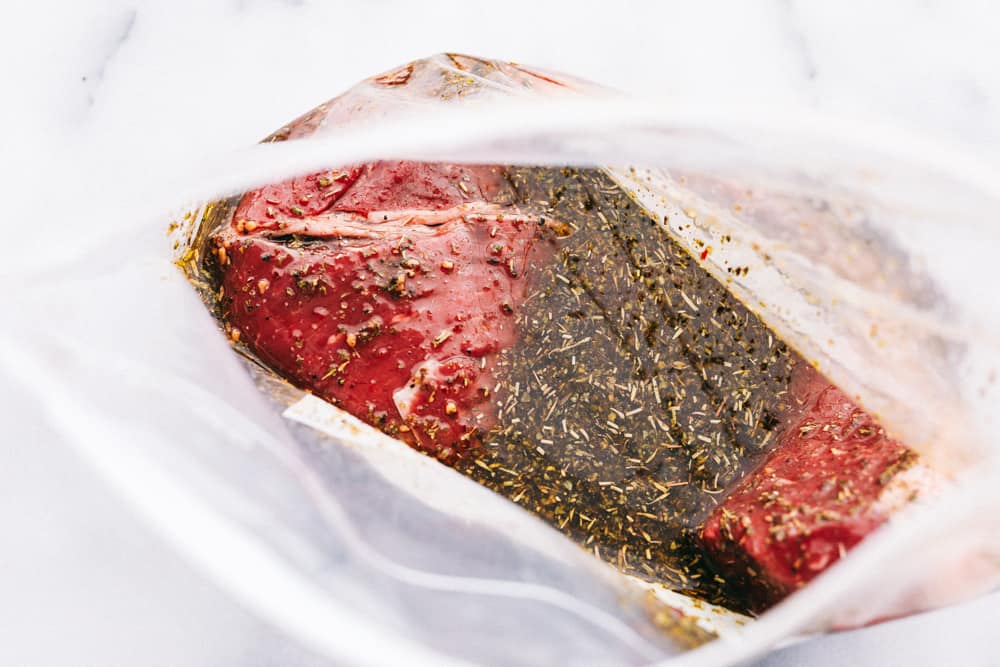 London Broil steak placed in a ziplock bag with a marinade over it. 