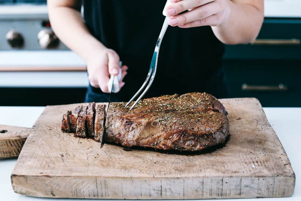 London Broil se coloca sobre una tabla de cortar de madera que se corta en pedazos con un cuchillo. 