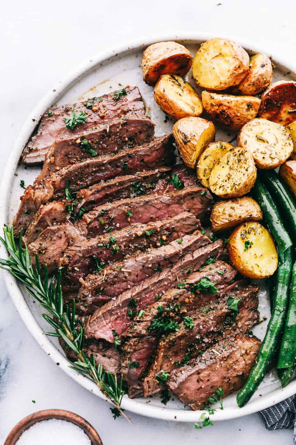 London Broil en rodajas en un plato con patatas asadas y judías verdes. 