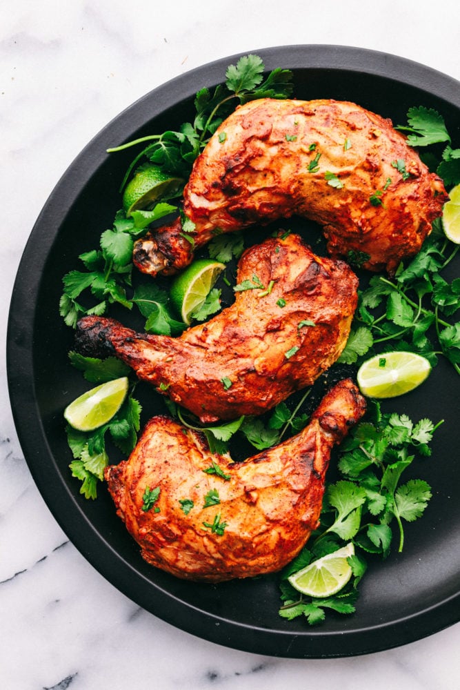 Tandoori chicken on a black plate with lettuce and lime wedges.