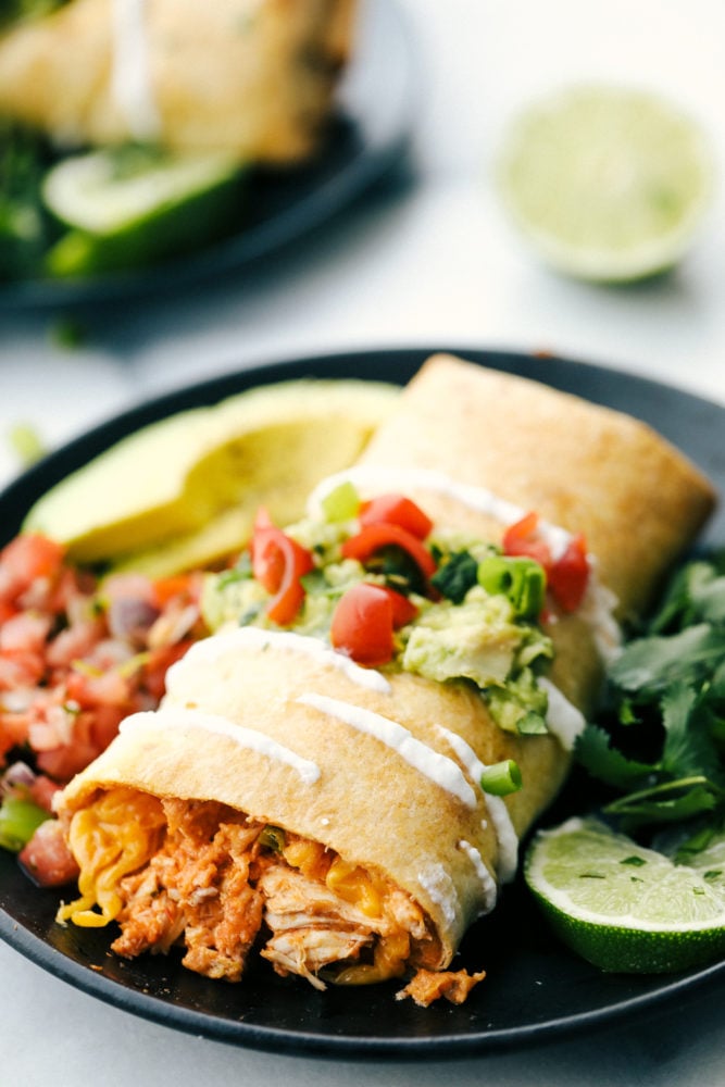 Chimichanga de pollo en un plato con salsa, aguacate y limas. 