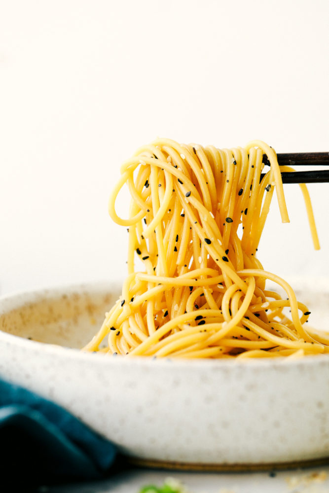 Garlic sesame noodles in a bowl being pulled up with chopsticks. 