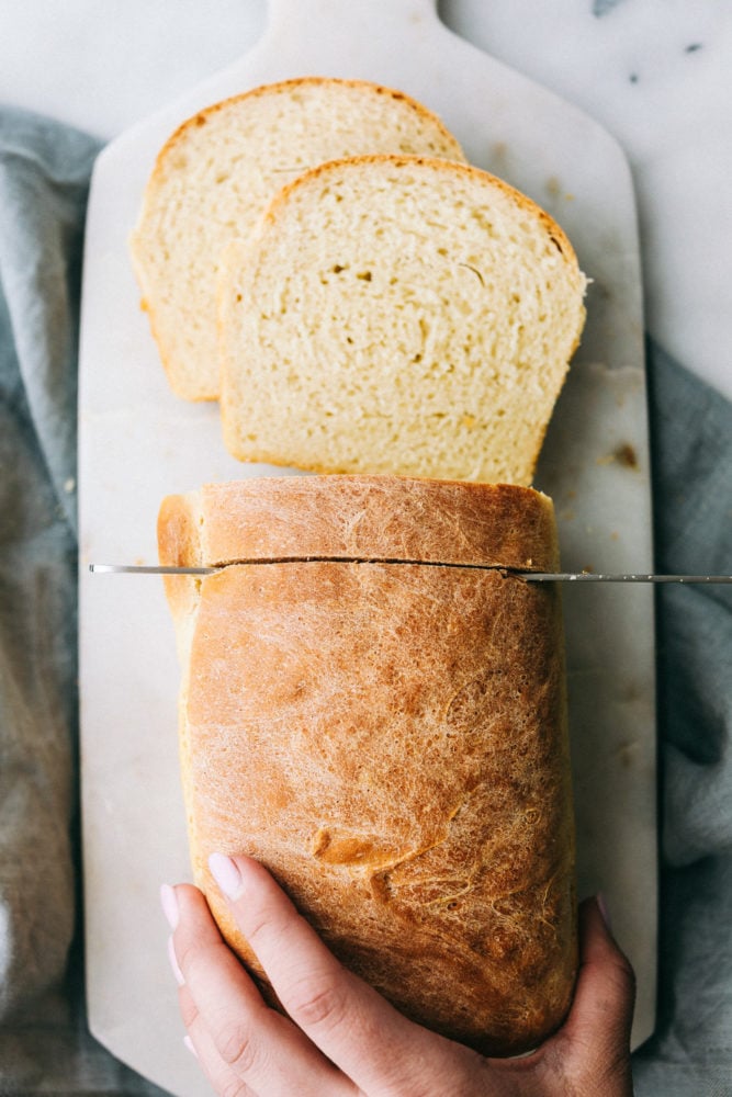 Overhead photo of a bread loaf being sliced with a knife.