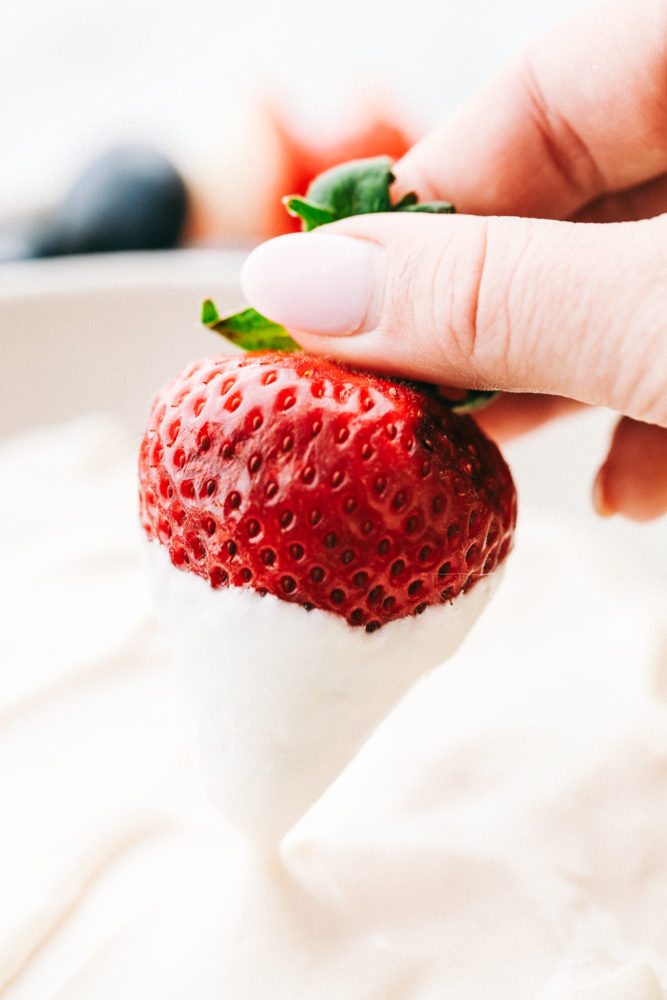 A red strawberry being dipped in marshmallow cream cheese fruit dip. 