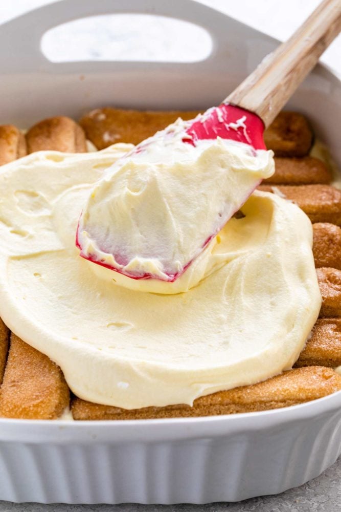 spreading filling mixture on ladyfingers sitting in a baking dish