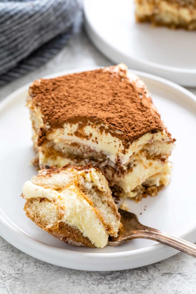 Slice of tiramisu on a plate with a spoonful taken out