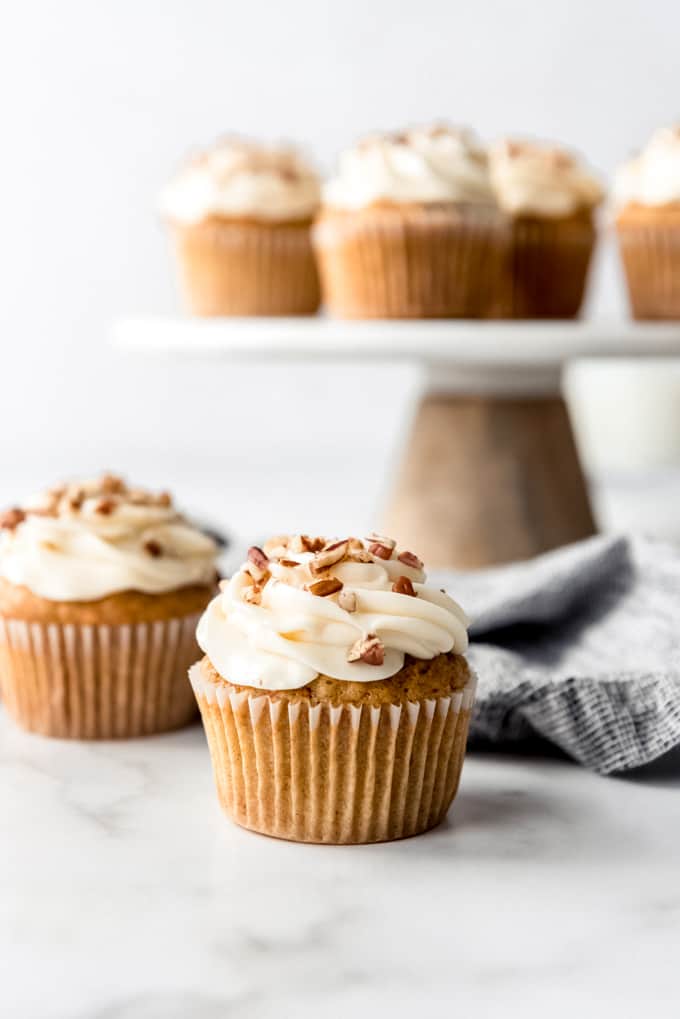 An image of carrot cake cupcakes with cream cheese frosting and pecans.