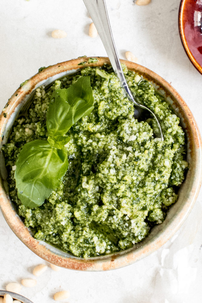 pesto sauce in pottery bowl with basil leaf and silver spoon