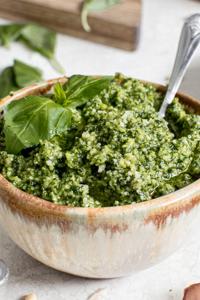 Basil pesto in a pottery bowl with a silver serving spoon.