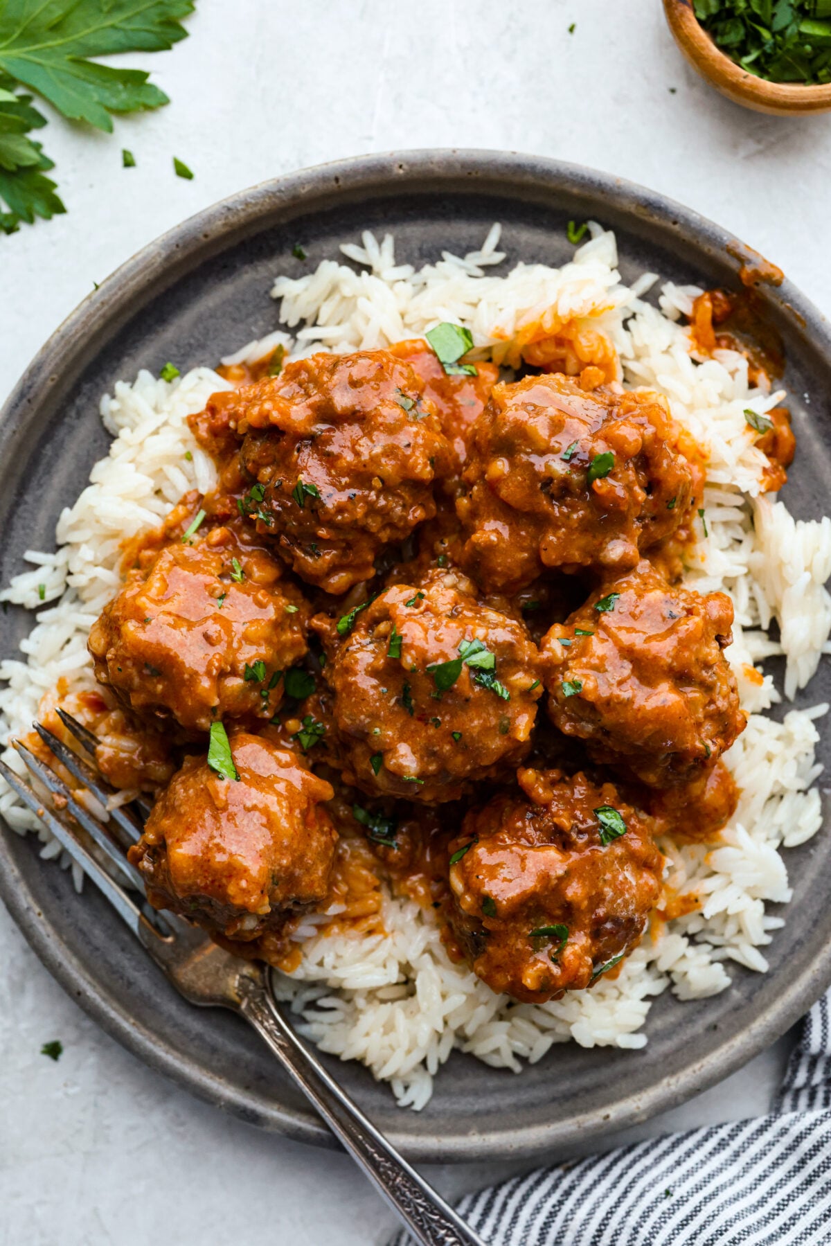 A plated photo of porcupine balls on some rice with a fork. 