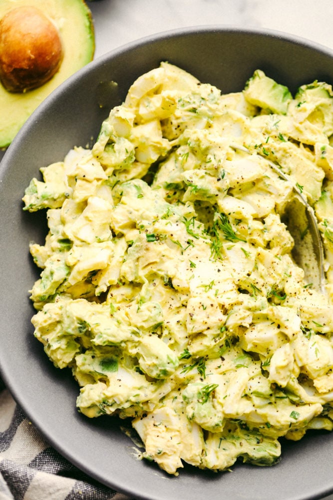 Avocado egg salad mixed together in a gray bowl with a spoon inside of it. 