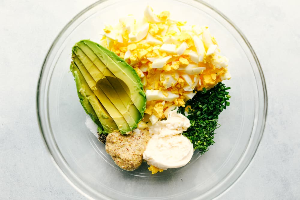 The ingredients to make avocado egg salad in a glass mixing bowl.