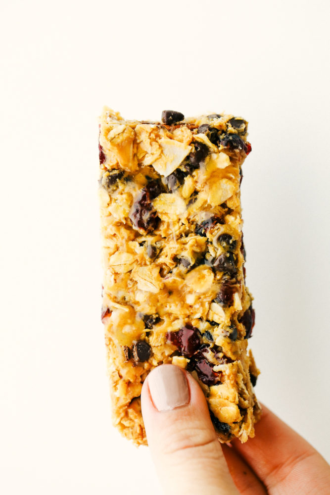 A granola bar standing up on a photo with a hand holding it. 