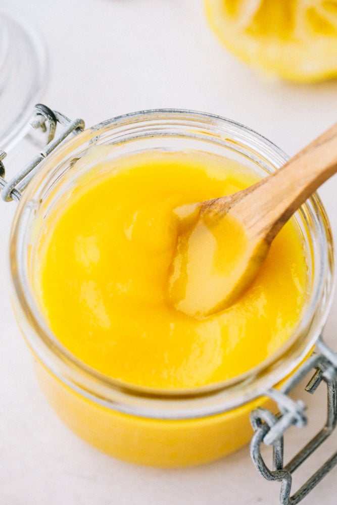 Lemon curd in a jar with a wooden spoon sitting in the curd resting on the side. 