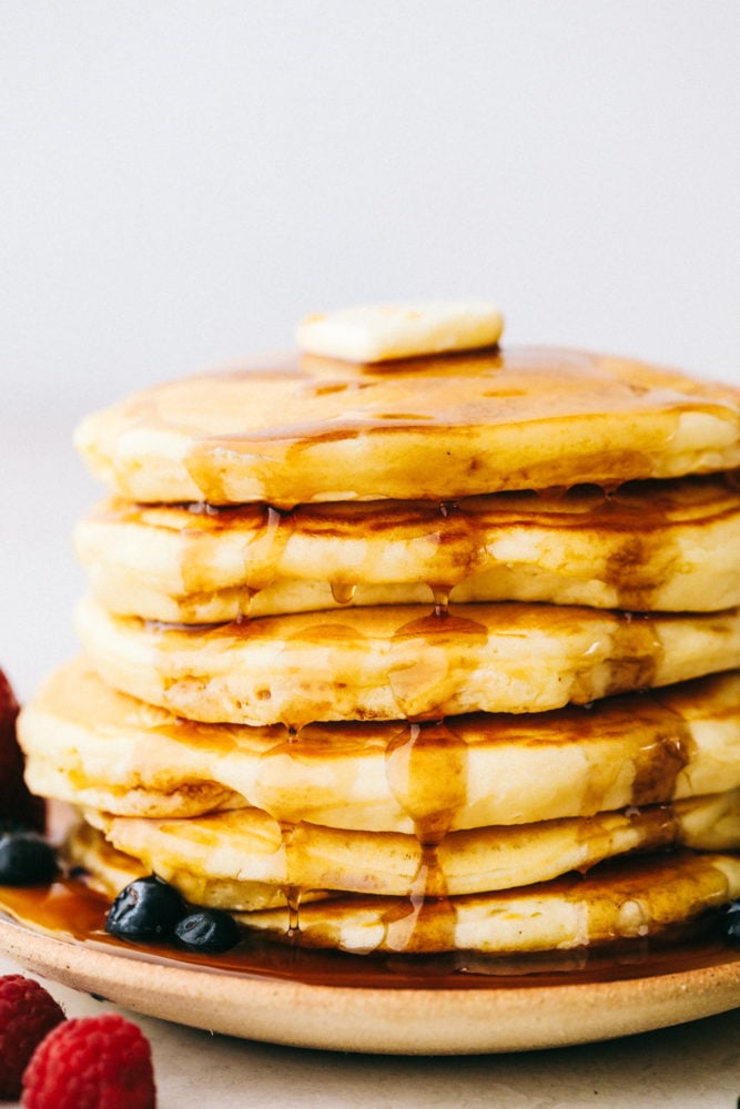 Fluffy pancakes stacked on top of each other with a slice of butter, syrup and fresh fruit. 