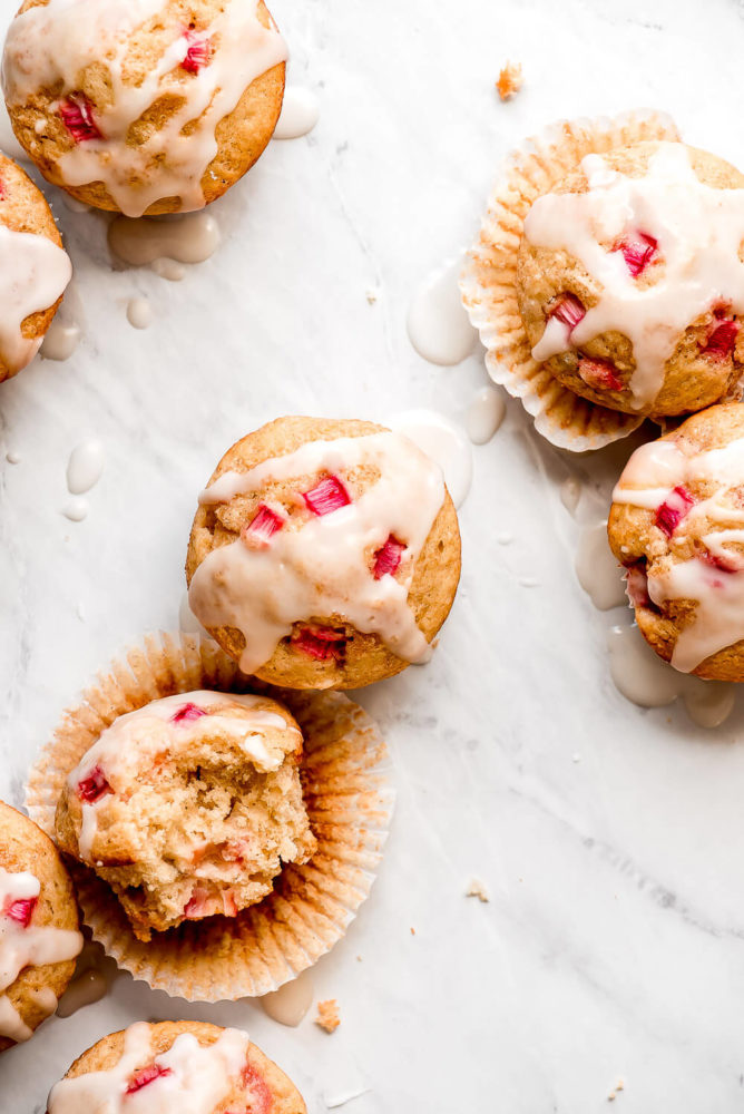 Rhubarb Muffins drizzled with a glaze and scattered on a marble surface.