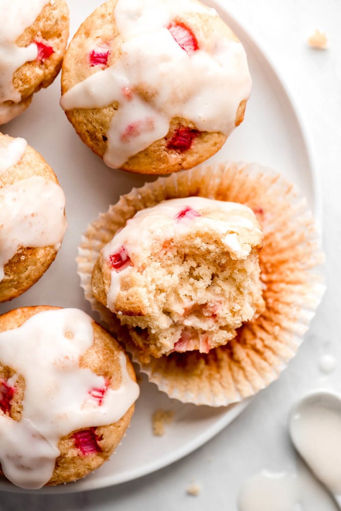 Glazed Rhubarb Muffins on a plate with one unwrapped and a bite taken out.