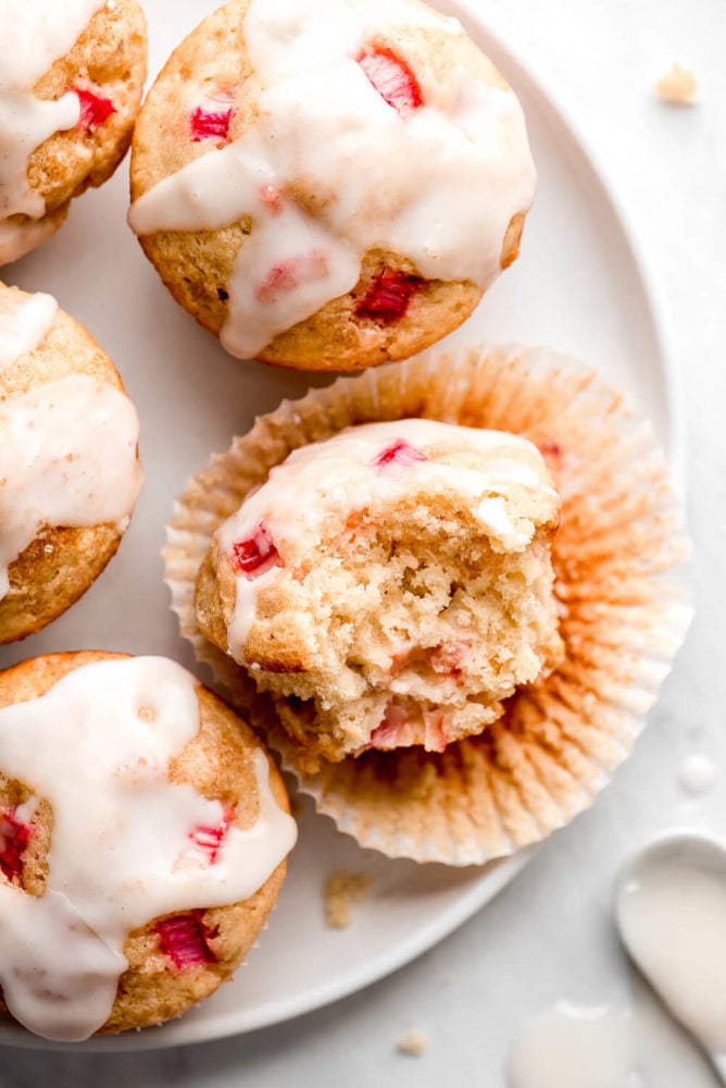 Muffins de ruibarbo glaseados en un plato con uno sin envolver y un bocado sacado.