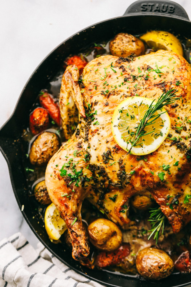 Garlic roasted chicken with vegetables on a skillet after being cooked and garnished with lemon on top. 