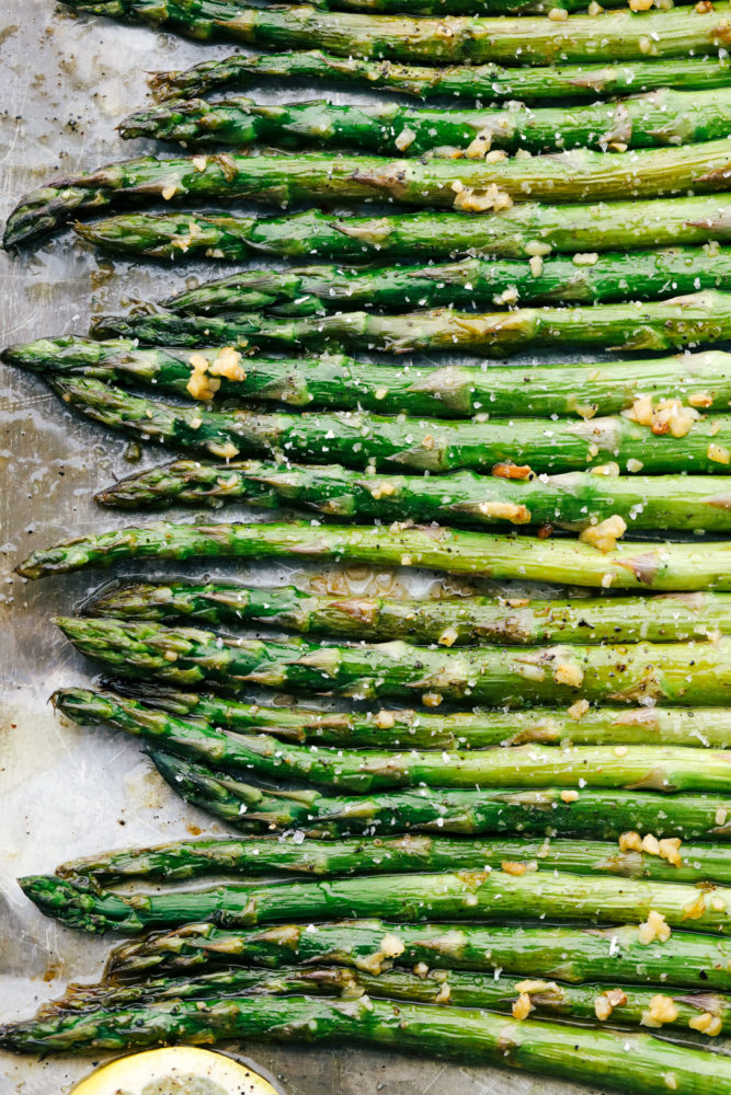 Asparagus laying flat on a baking sheet showing just he heads of the asparagus. 