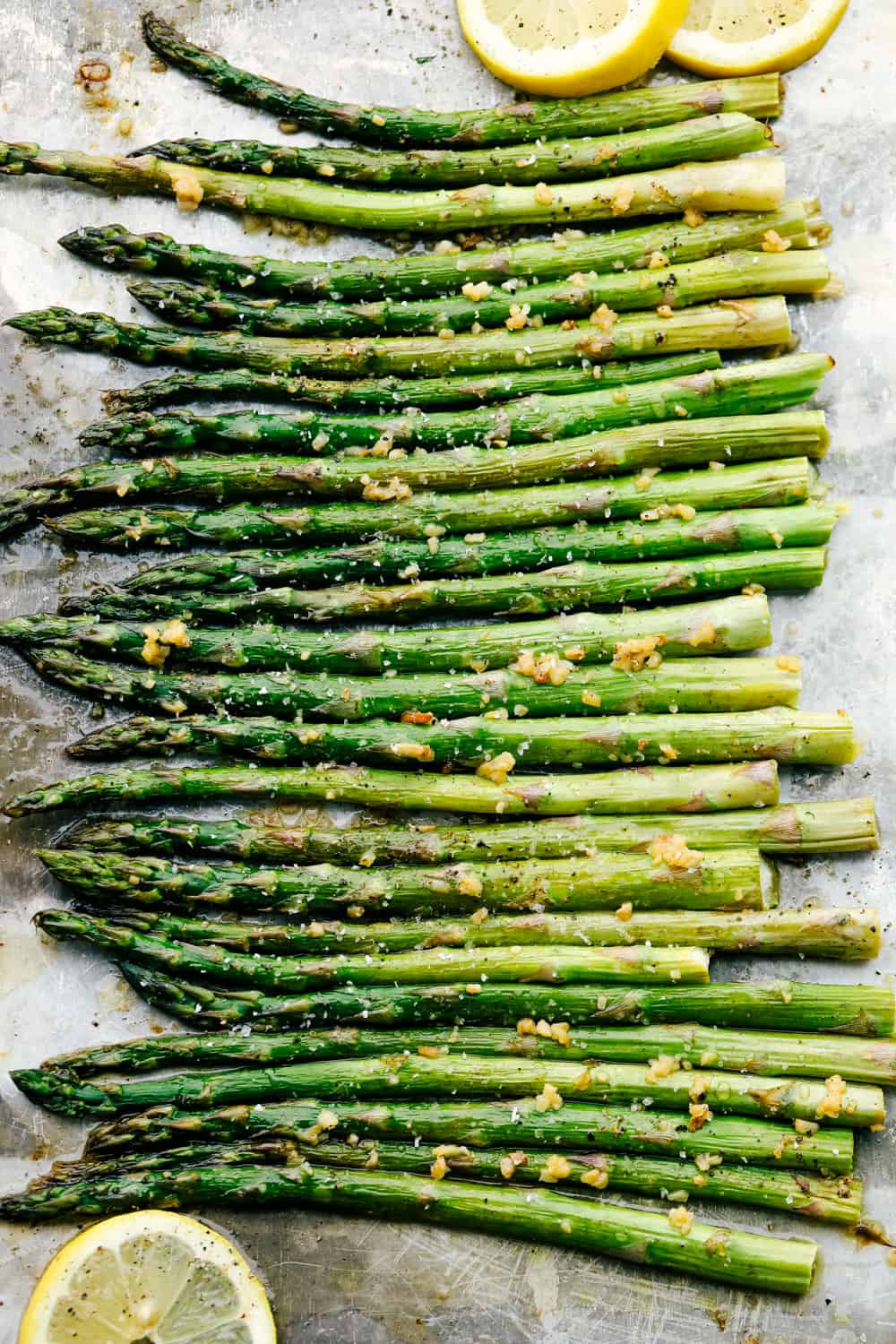 Asparagus all lined up flat on the baking sheet with lemons garnished around them. 