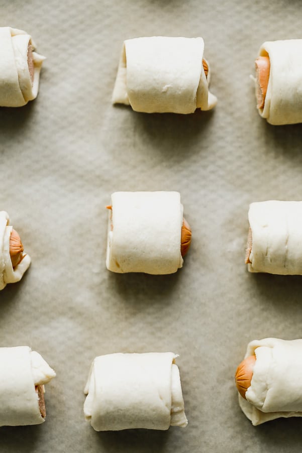 Pigs in a blanket on a sheet pan getting ready to be baked.